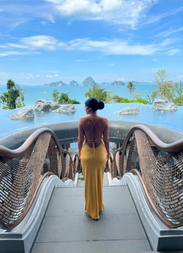 Shani in a yellow dress on a bridge over an infinity pool facing limestone islands