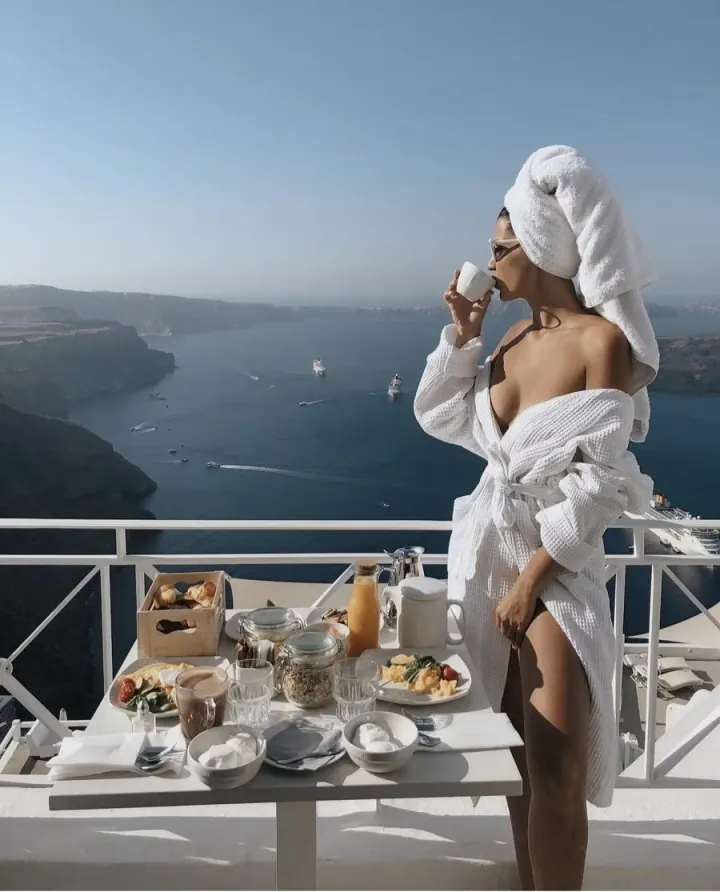 Shani in a robe and towel sipping coffee on a balcony above the Santorini caldera