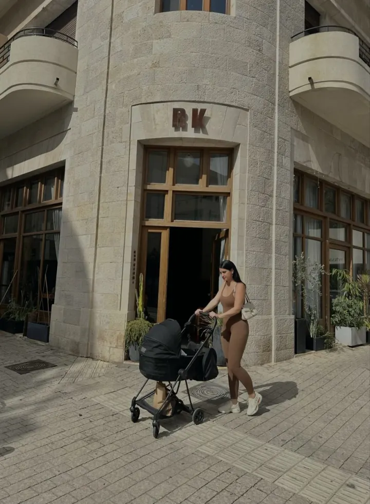 Shani pushing a stroller past a stone building on a street corner