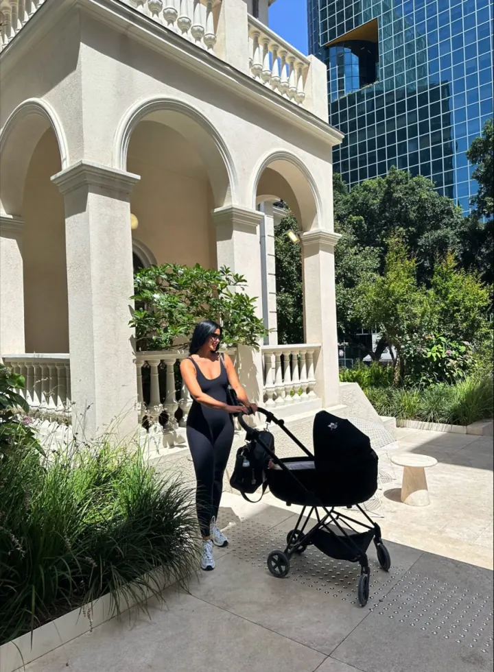 Shani pushing a stroller through a garden courtyard with white arches