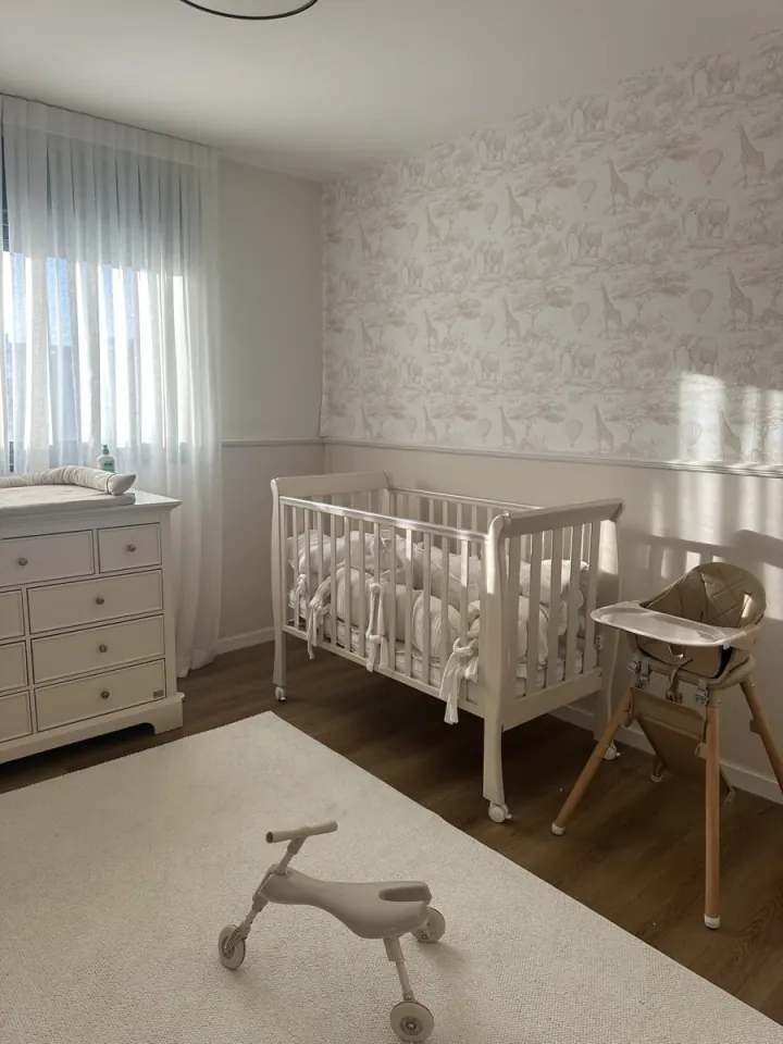Nursery with patterned wallpaper, a white crib, a high chair and a balance bike
