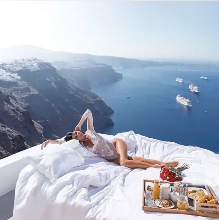 Shani lounging on a white daybed with breakfast above the Santorini caldera